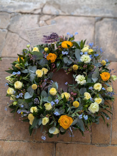 Spring Remembrance Wreath - A beautifully handcrafted wreath in soft yellow, ivory, blue and lavender tones, thoughtfully arranged with seasonal flowers and fresh foliage.