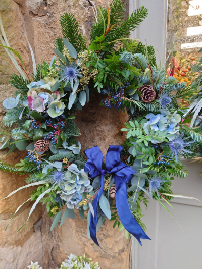 Blue Christmas Wreath - A handcrafted Christmas wreath featuring fresh seasonal foliage, blue hydrangeas, pinecones and a luxurious ribbon for an elegant festive display.
